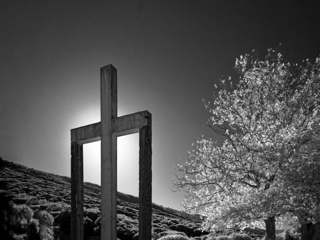 A concrete cross hides the sun in this black and white photo. The supports for the two arms make a strange design, almost like a peculiar "Π".