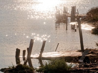 A photograph depicting two small wooden piers with the glare of the sun on the sea serving as the background.