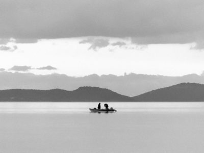 Two fishermen in a boat fishing at dusk. The calm waters and the scenery might look like a lake but it really is the sea.
